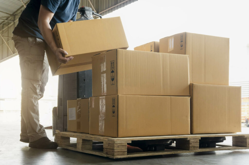 Worker courier lifting shipment boxes stacking on pallet.